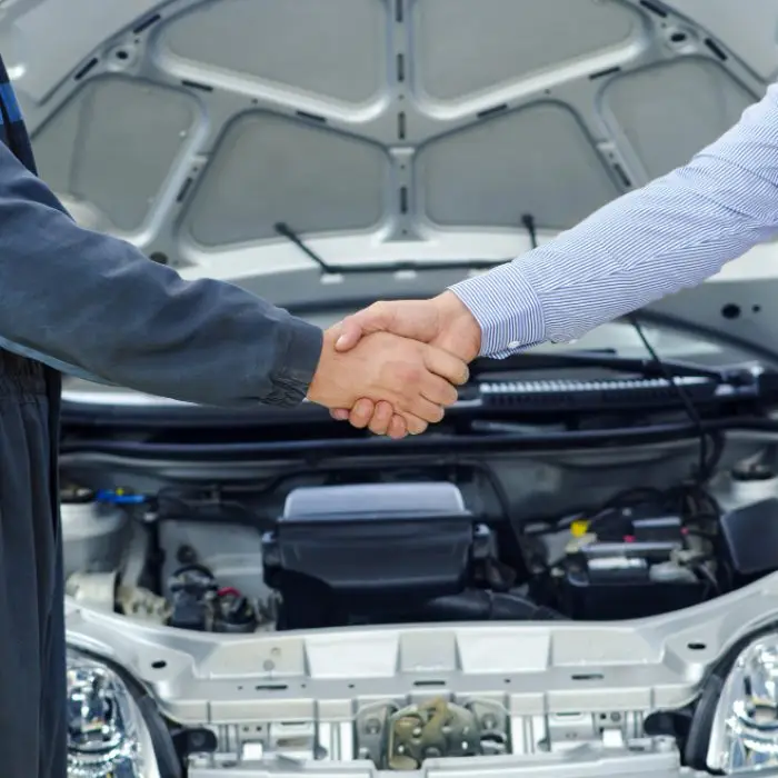 Car Repair Service Agreement Between Mechanic and Customer Mechanic shaking hands with customer after car repair with open hood